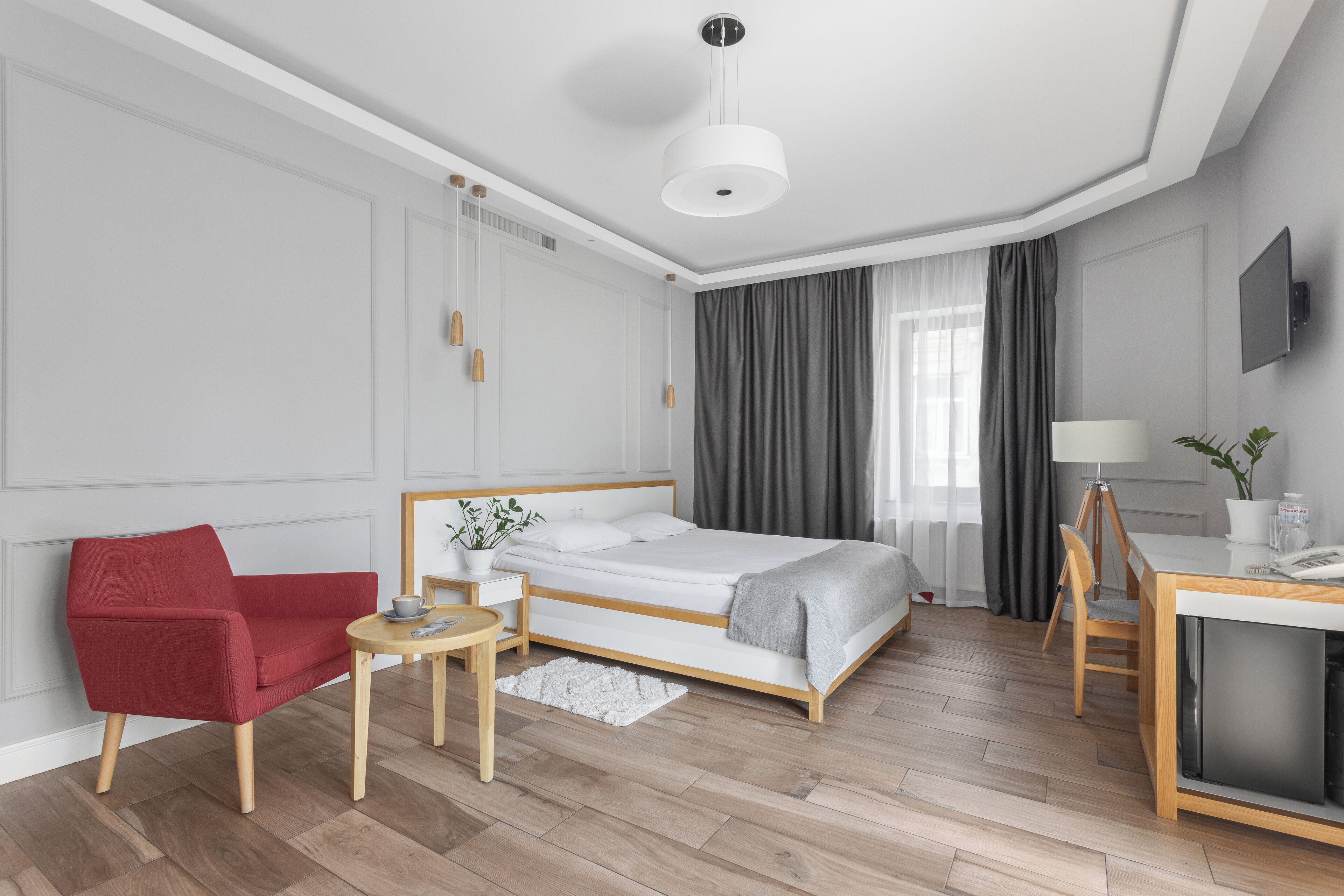 A modern hotel room with a bed, a red armchair, a desk, and a TV.