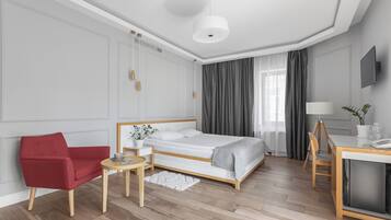 A modern hotel room with a bed, a red armchair, a desk, and a TV.