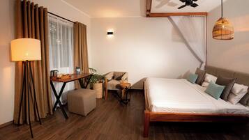 A hotel room with a bed, a desk with a lamp, a chair, a small table, and a ceiling fan.