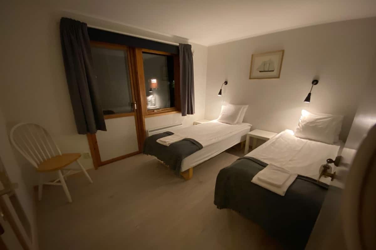 A hotel room with two single beds, a chair, a small table, and a window with curtains.