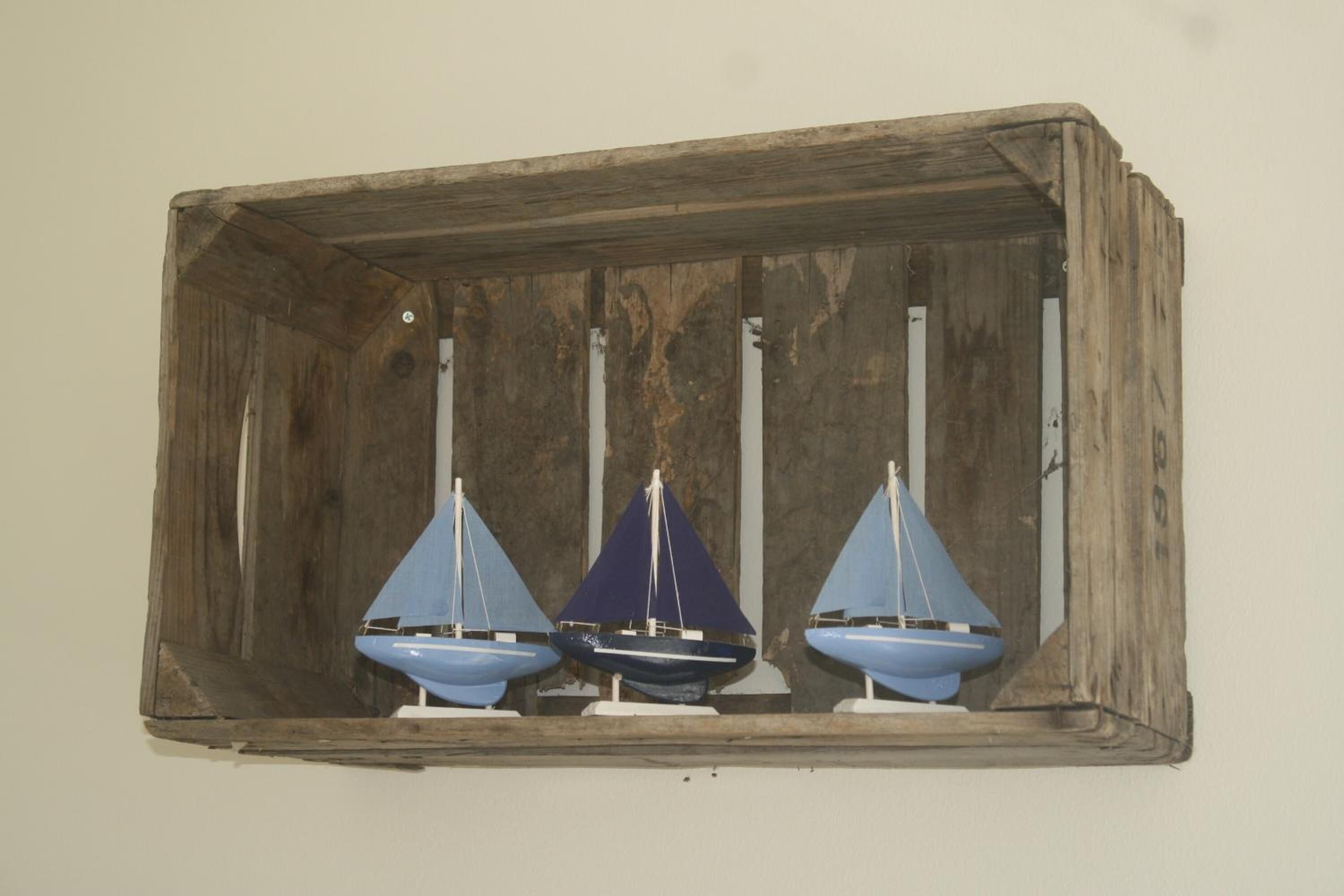 Une étagère en bois rustique sur laquelle sont posés trois petits voiliers.