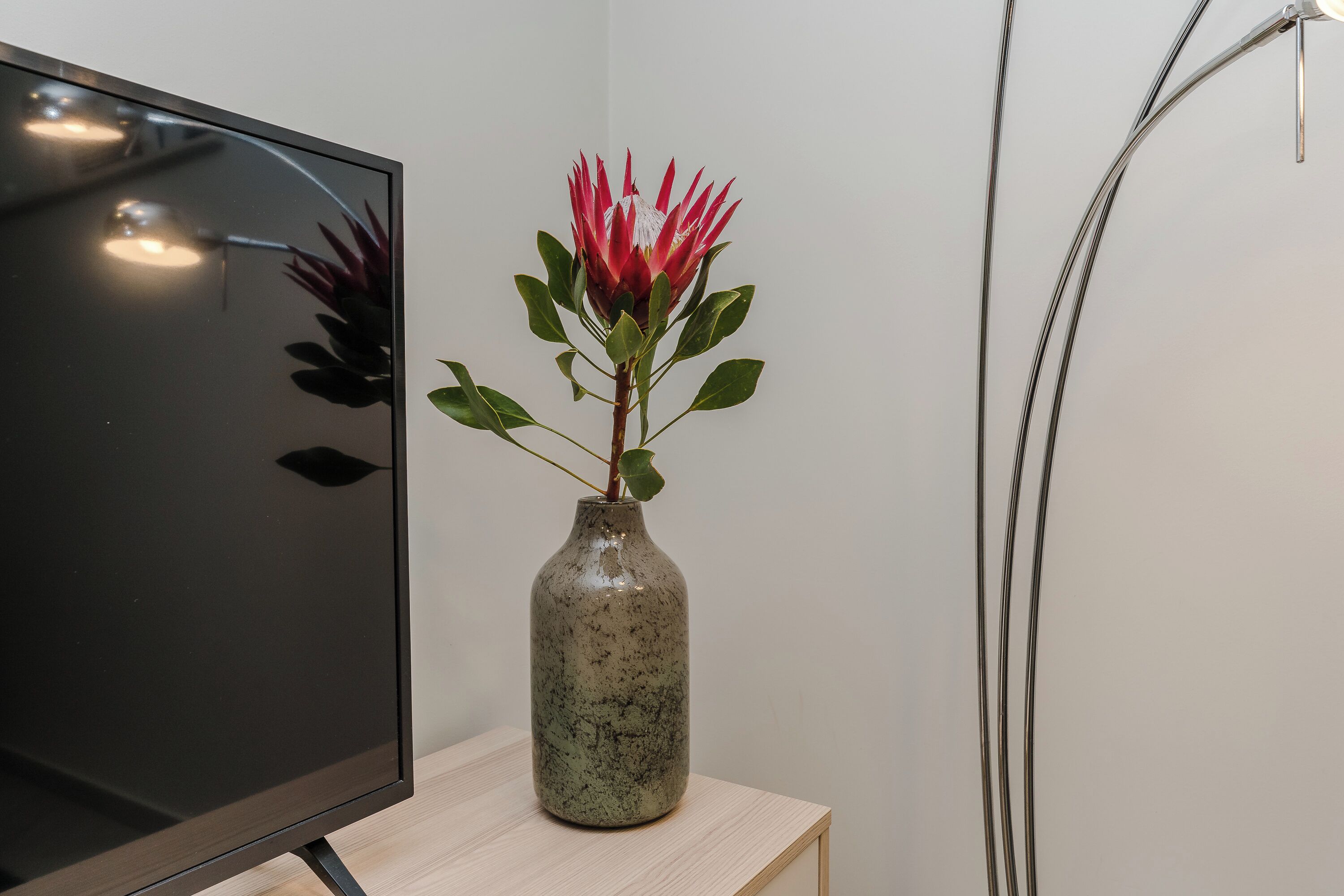 Un téléviseur posé sur un meuble en bois, avec un vase en céramique contenant une fleur rouge.