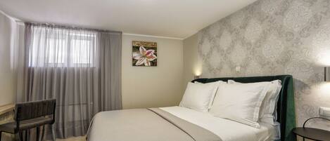 Una habitación de hotel con cama, sillón, escritorio y ventana con cortinas.
