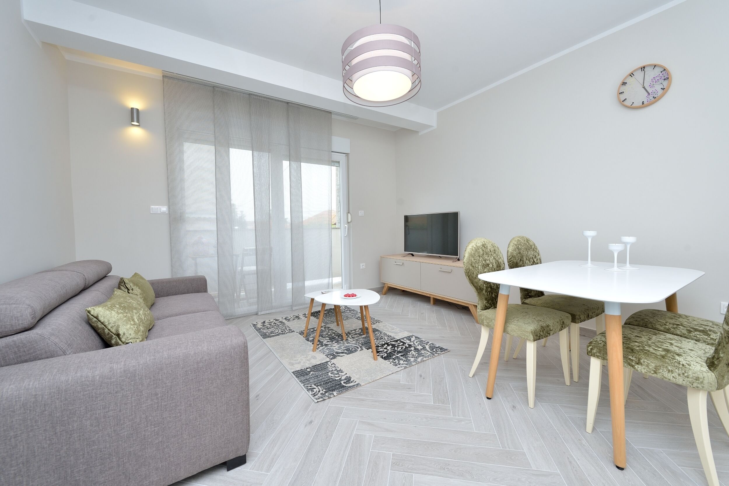A modern living room with a grey sofa, a small round table, and green upholstered chairs.