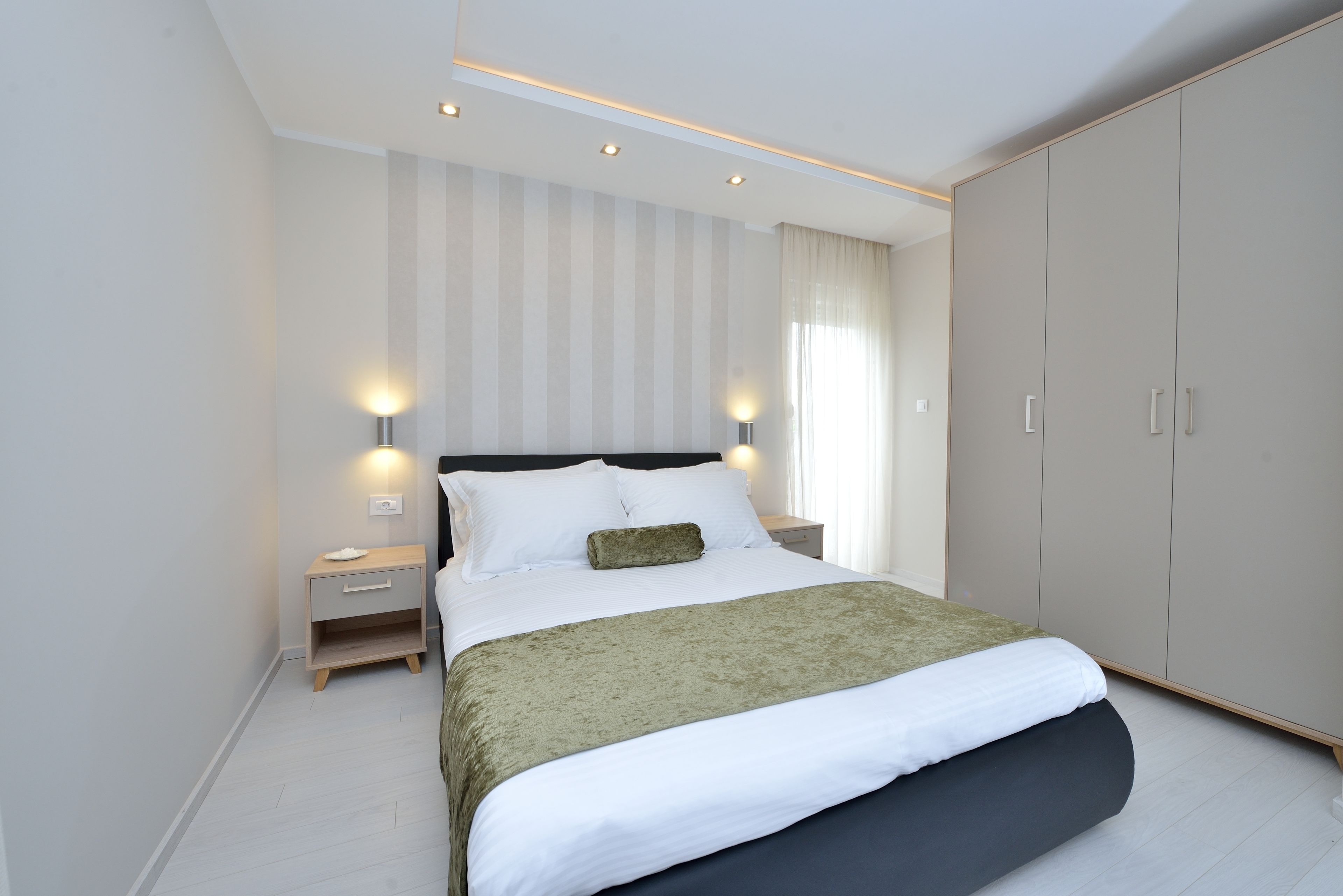 A modern bedroom with a large bed, a nightstand, a wardrobe, and two wall-mounted lights.