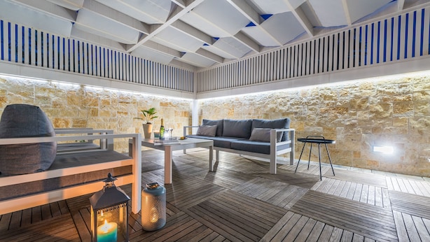 An outdoor patio with a stone wall, wooden flooring, a white sofa, a small table, and a lantern. - Apartments Villa Karla (Zadar)