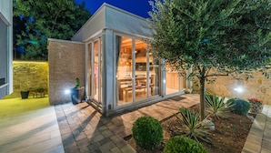A modern house with a glass door leading to a dining area, surrounded by a garden with various plants and a tree. - Apartments Villa Karla (Zadar)