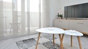 A modern living room with a large TV, two white tables, a patterned rug, and a sliding glass door. - Apartments Villa Karla (Zadar)