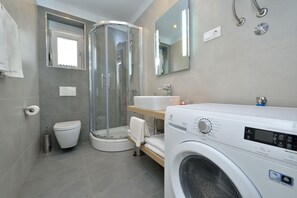 Un baño moderno con cabina de ducha de vidrio, inodoro, lavamanos y lavadora.