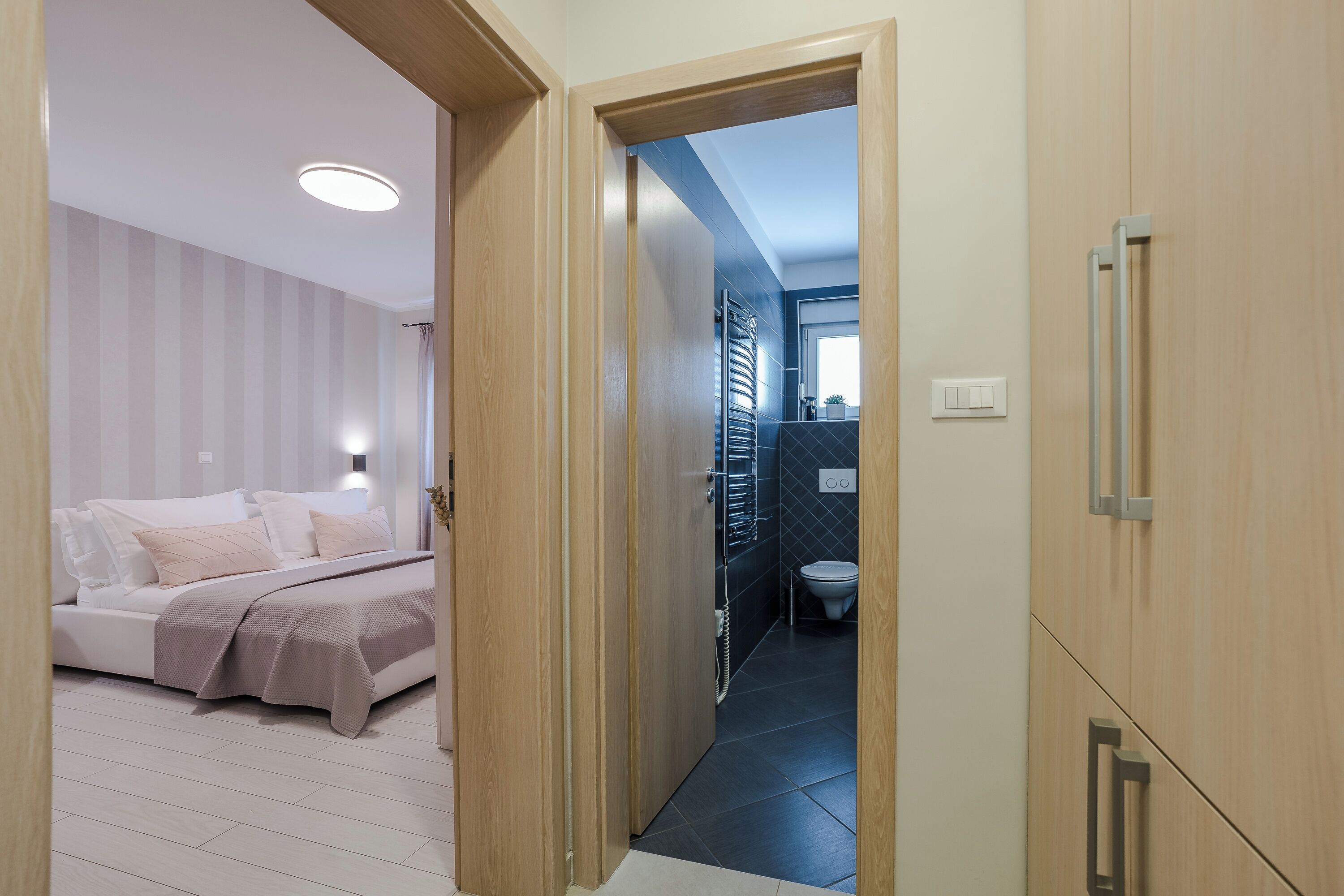 A bedroom with a bed, a bedside table, and a nightstand. There is a door leading to a bathroom with a toilet and a shower.