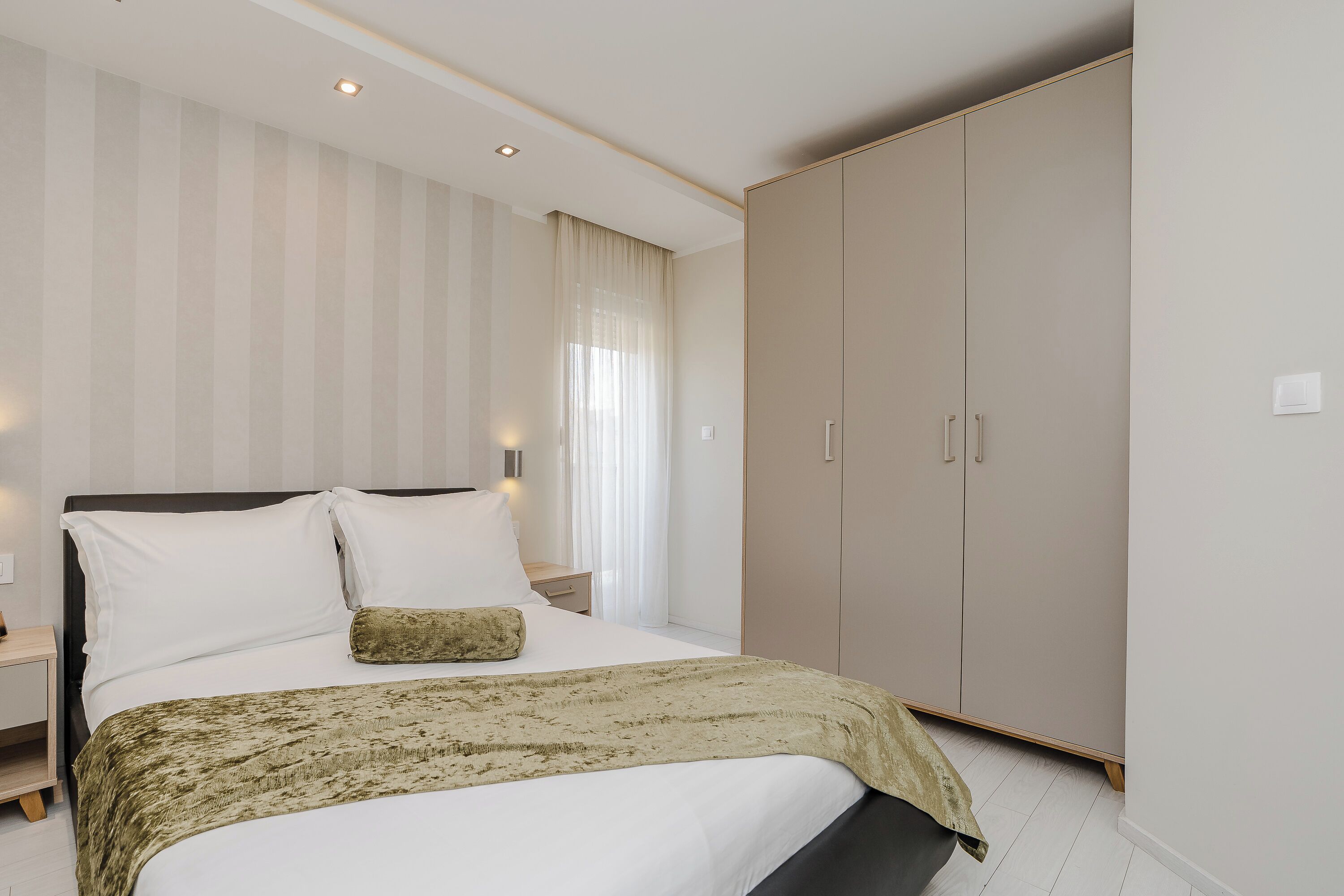 A bedroom with a bed, nightstands, a wardrobe, and a window with curtains.
