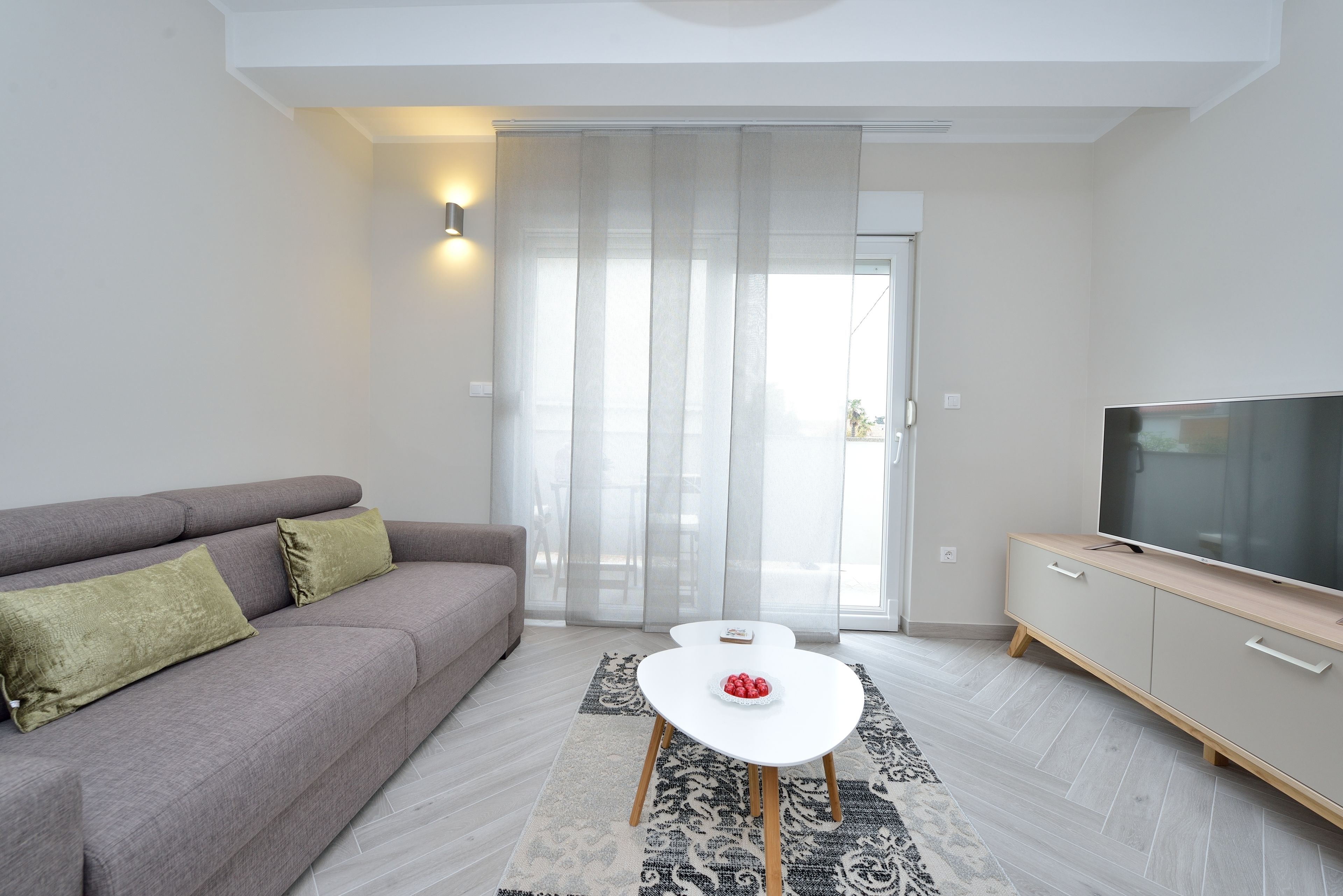 A modern living room with a grey sofa, a white coffee table, and a TV on a wooden cabinet.