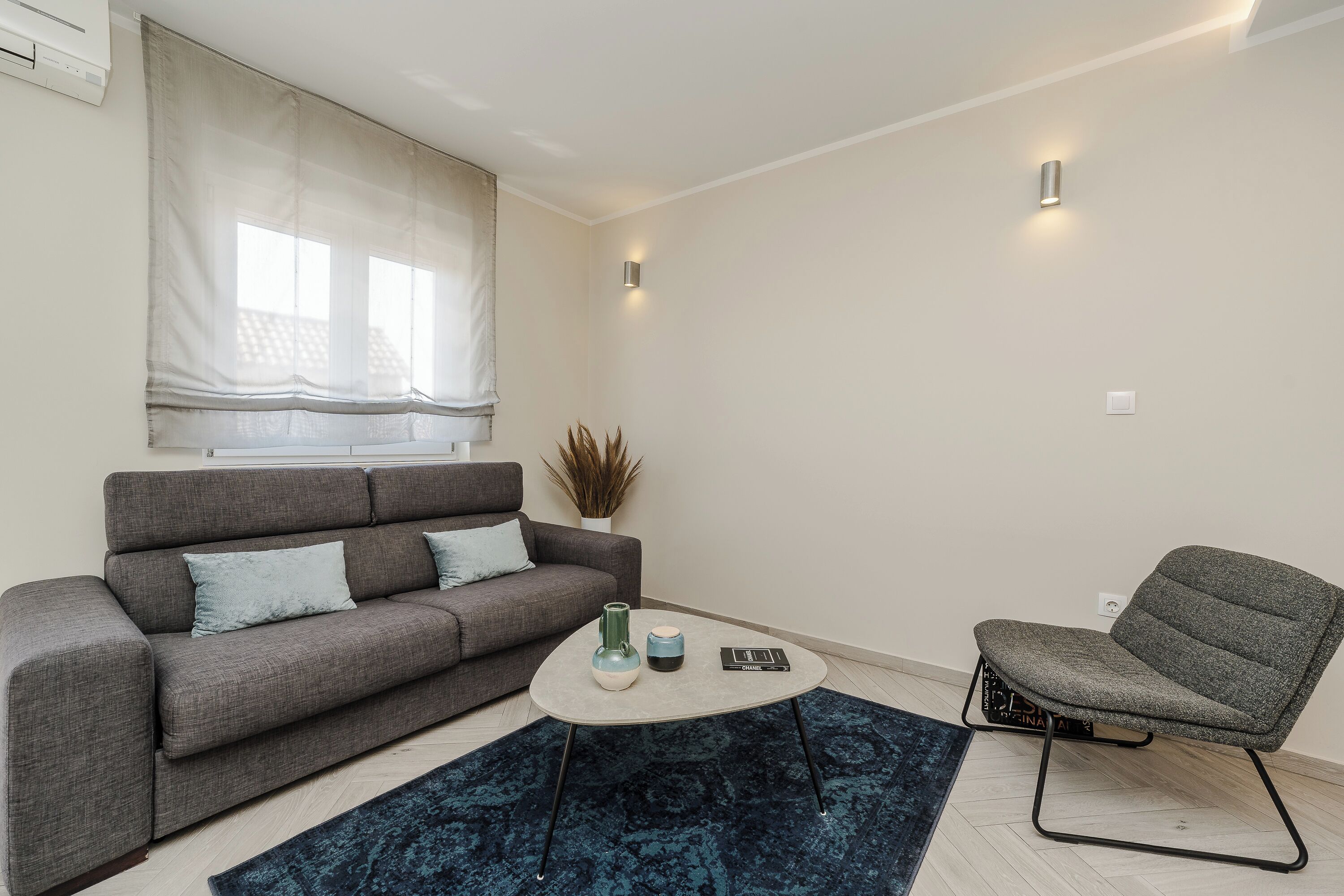 Un salon moderne avec un canapé gris, un fauteuil assorti, une table basse et un tapis à motifs.