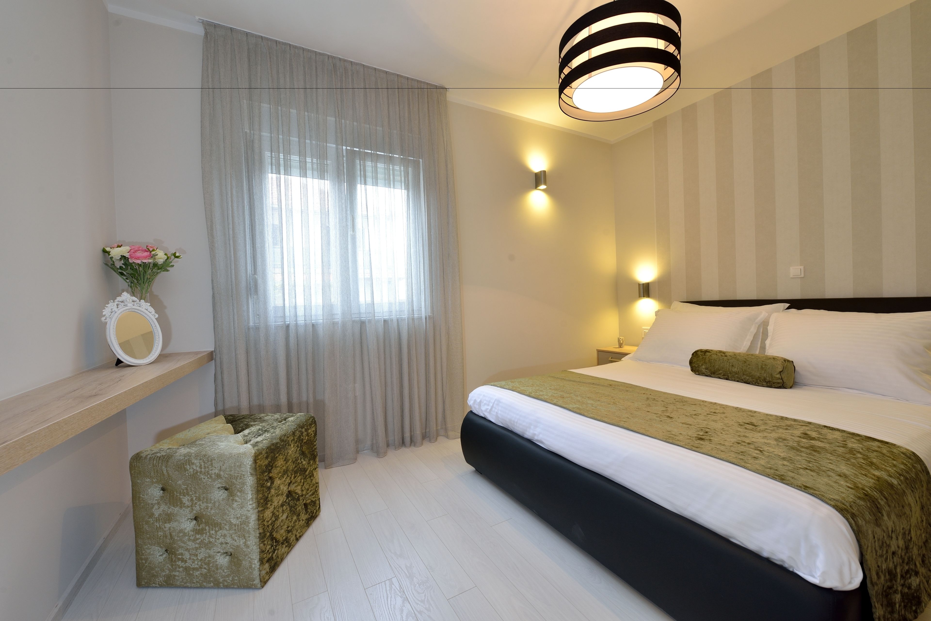 A modern hotel room with a large bed, a bedside table, a mirror, and a window with curtains.