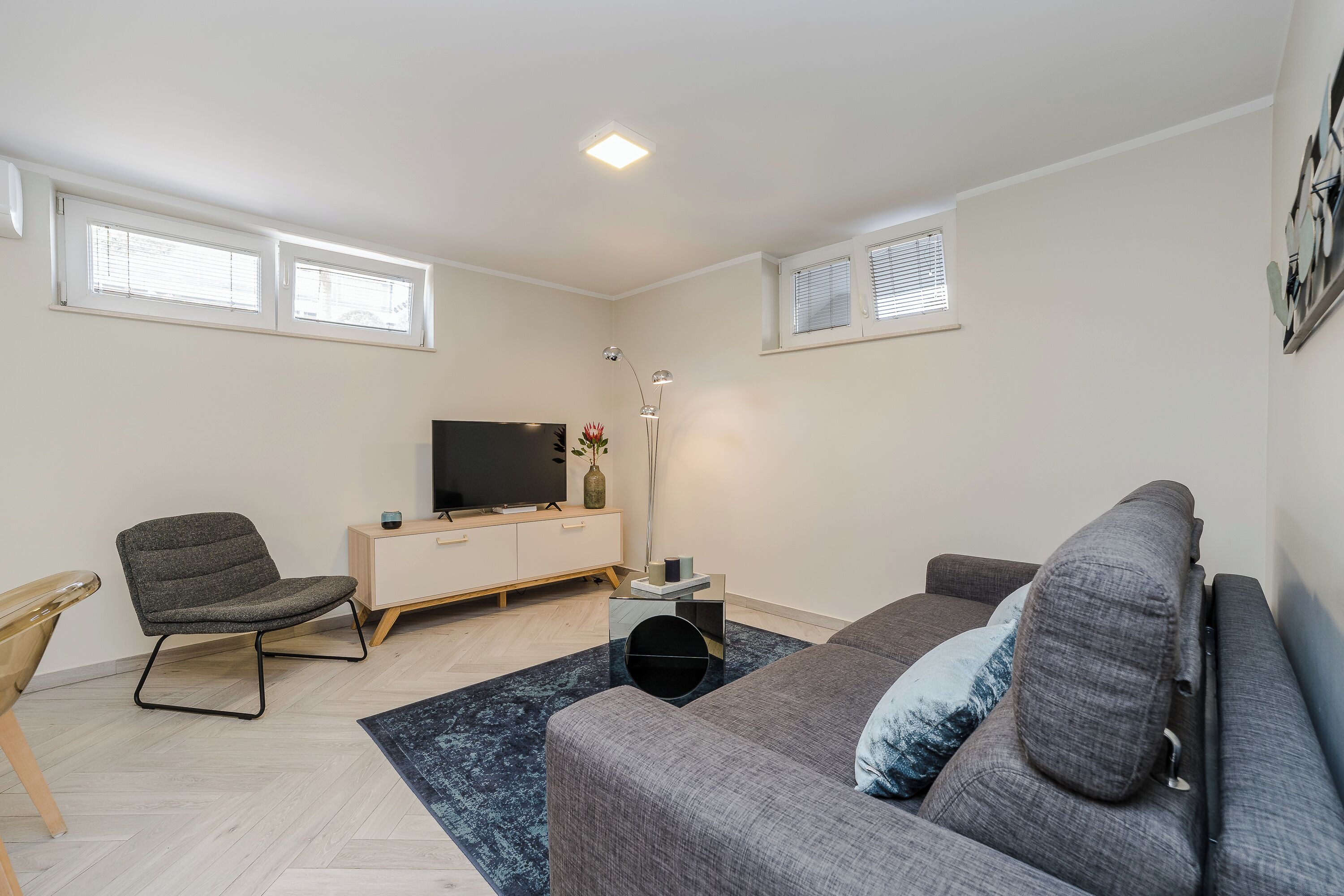 Una sala de estar moderna con un sofá gris, un mueble de madera, un televisor y una lámpara de pie.