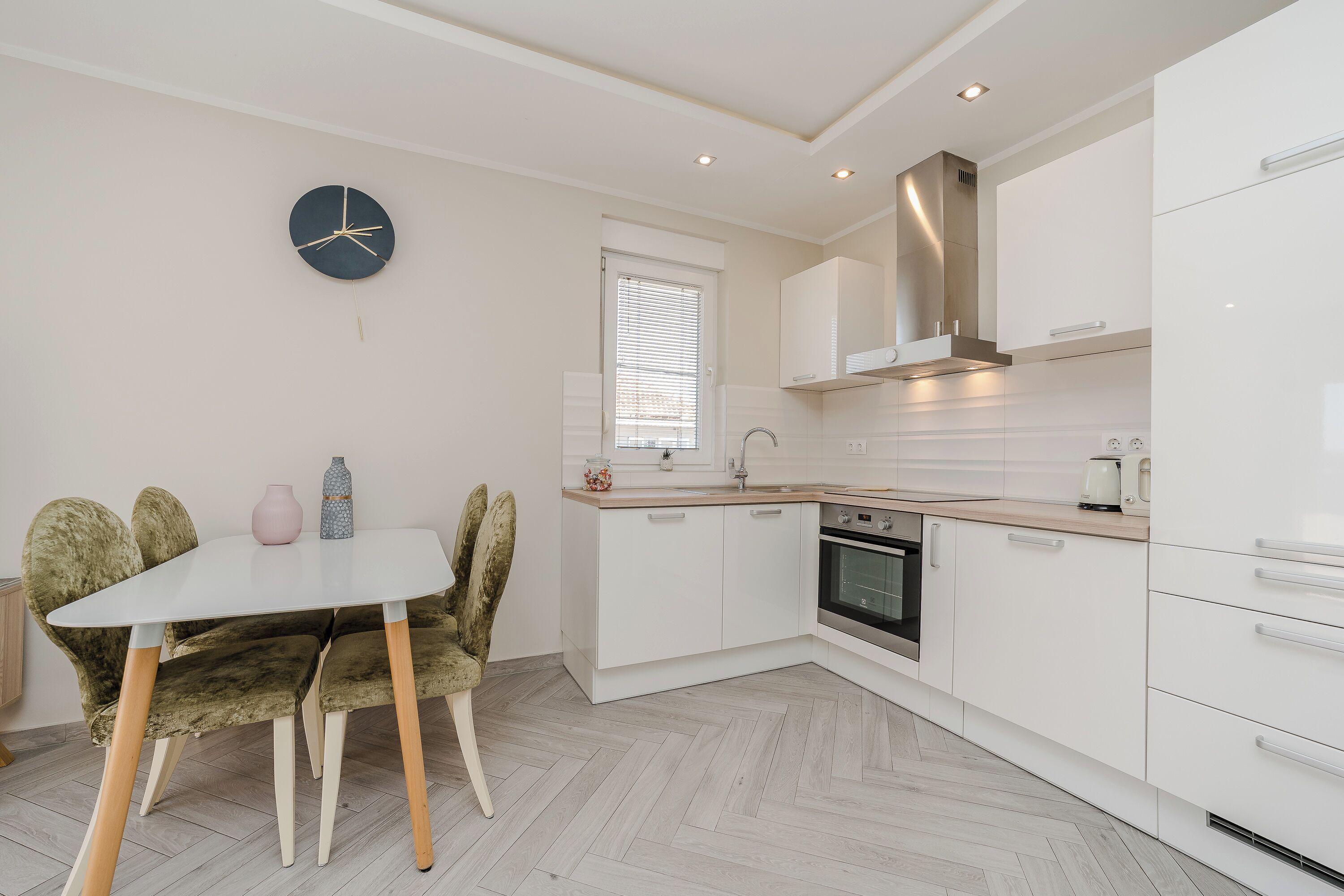 A modern kitchen with white cabinets, a built-in oven, and a herringbone-patterned floor.