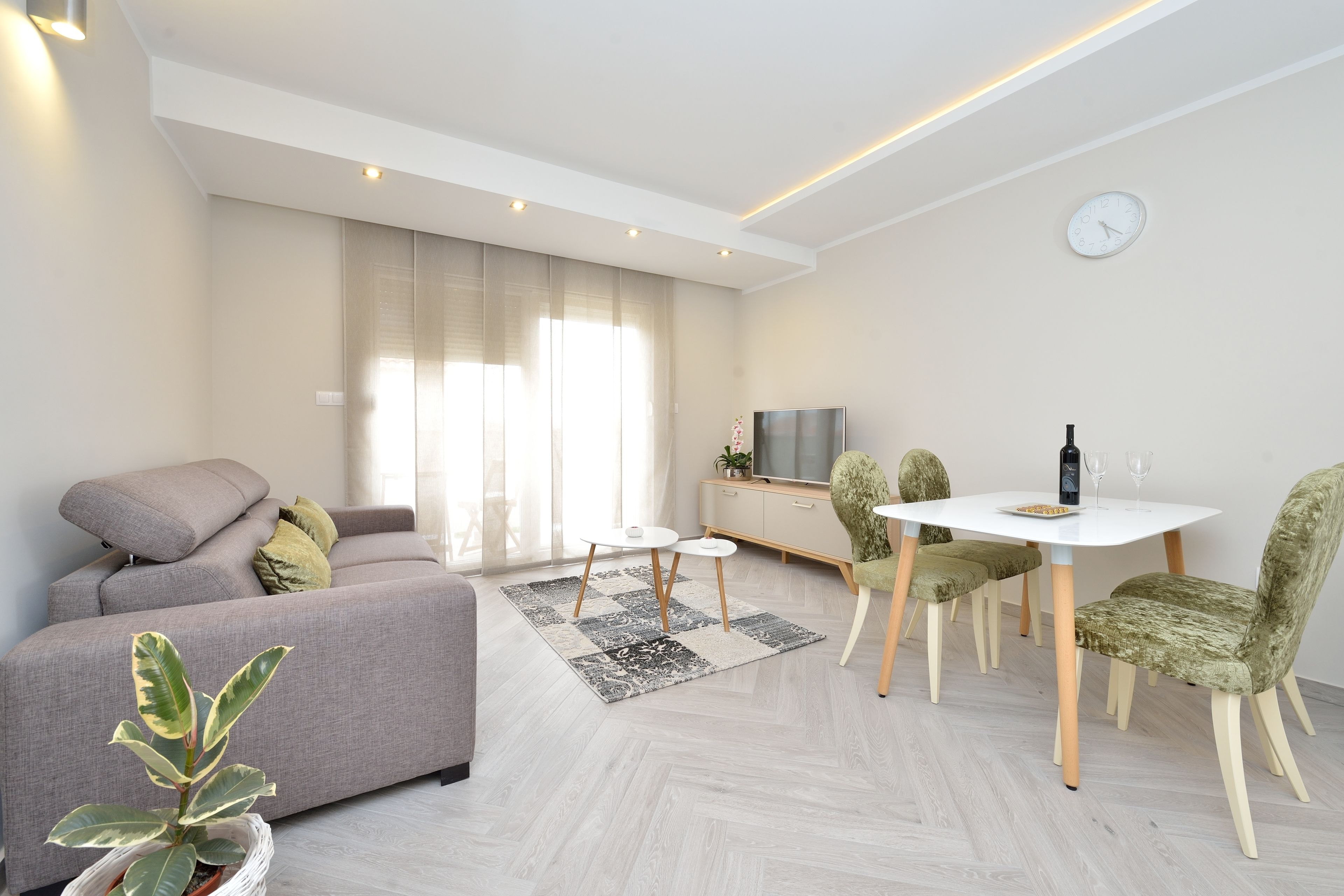 A modern living room with a sofa, a dining table with chairs, a TV, and a plant.