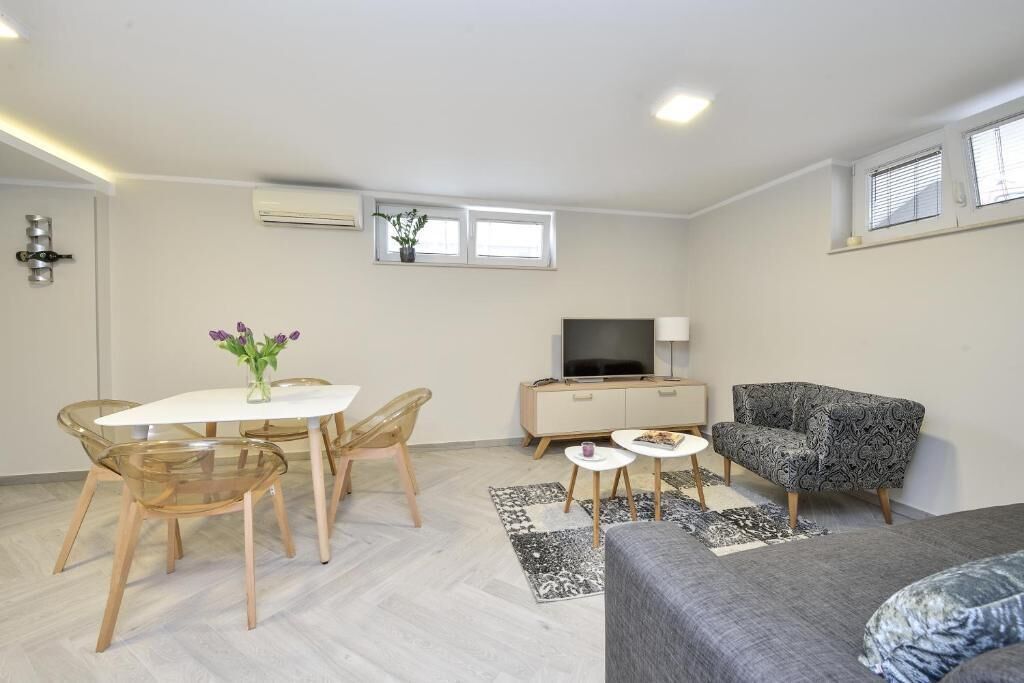 Een moderne woonkamer met een grijze bank, een eettafel met stoelen, een televisie en een fauteuil met een patroon.