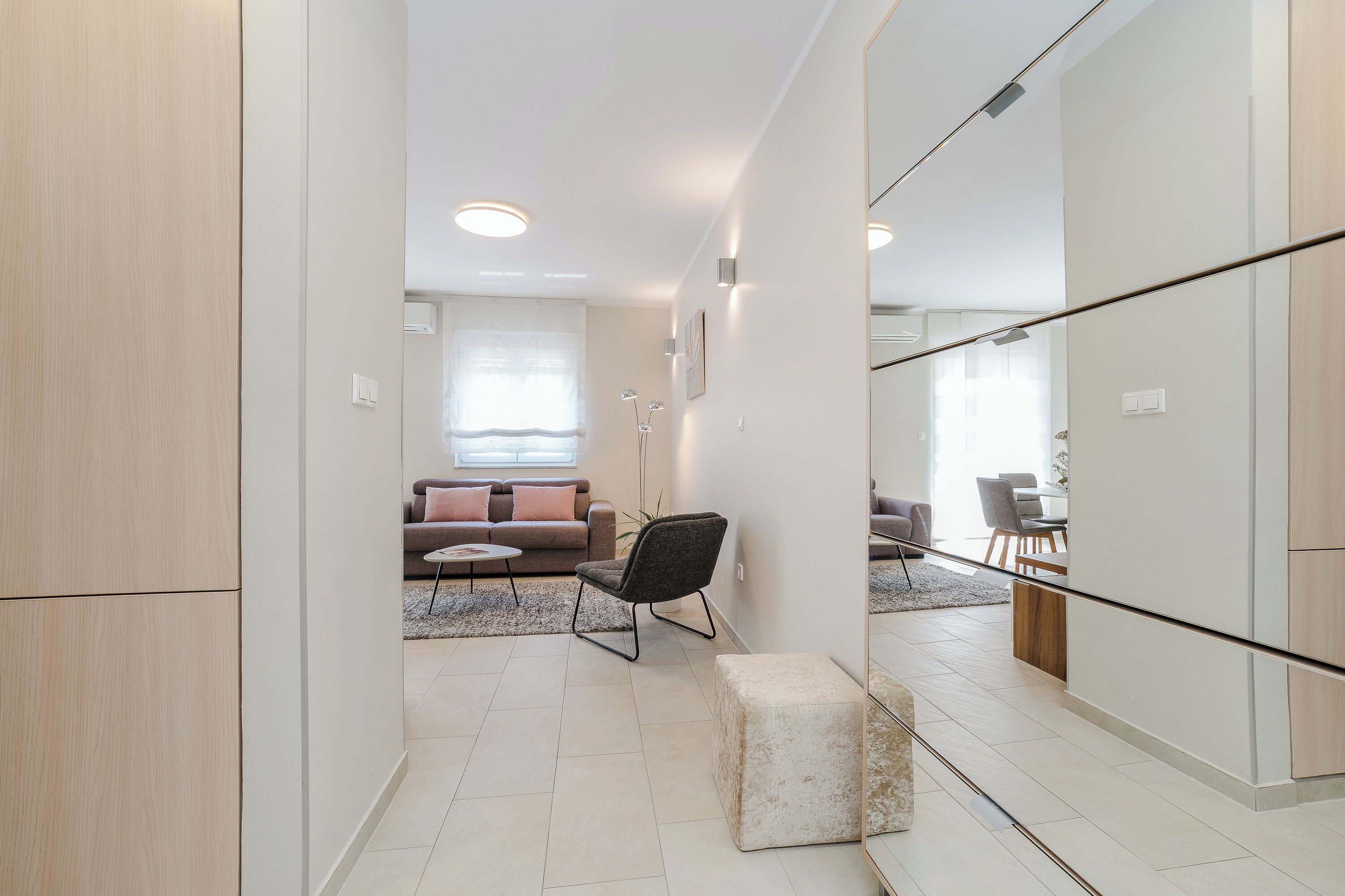 A modern living room with a sofa, a chair, and a small table. There is a large mirror on the wall and a wooden cabinet.