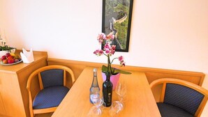 A dining area with a wooden table, two blue cushioned chairs, a vase with pink flowers, a bottle of water, and wine glasses. - Boardinghouse Hähn (Koblenz)