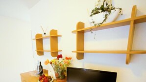 A living room with a wooden TV stand, a flat-screen TV, a vase with flowers, and a small shelf with a plant. - Boardinghouse Hähn (Koblenz)