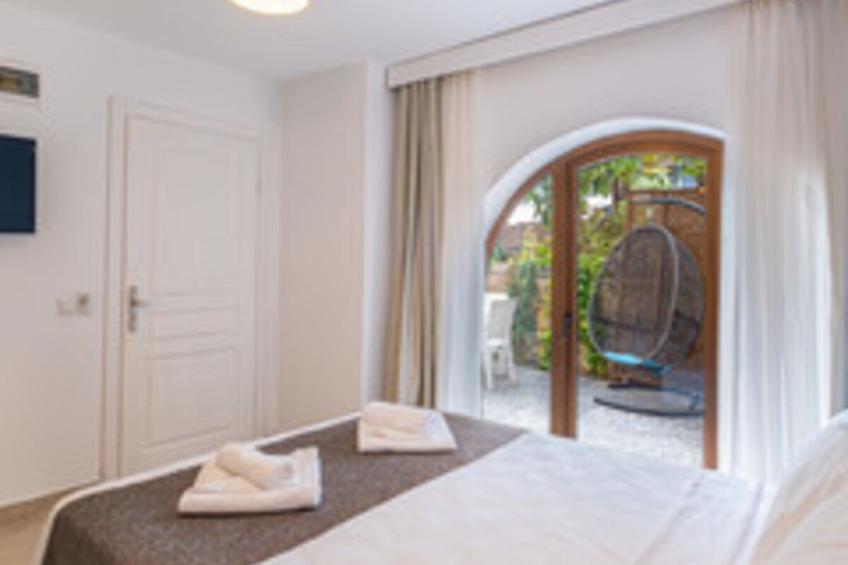 A hotel room with a bed, a small table, a chair, and a view of the outside.