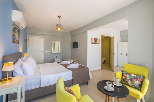 Une chambre d’hôtel comprenant un lit, un bureau avec une lampe, une chaise, une petite table avec des tasses et une porte donnant sur une salle de bain.