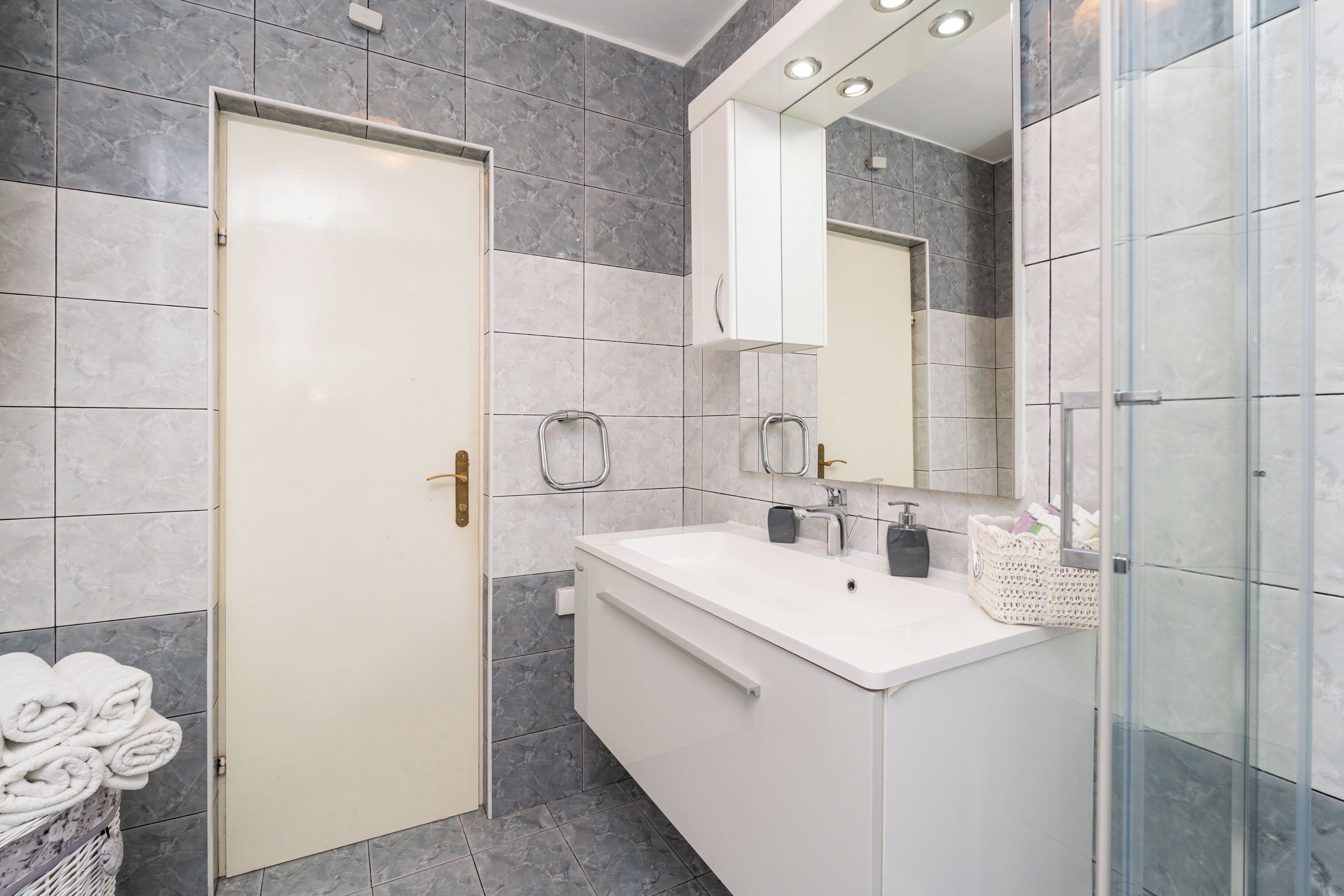 Een moderne badkamer met een wit badkamermeubel, een douchecabine van glas en een vloer van marmer.