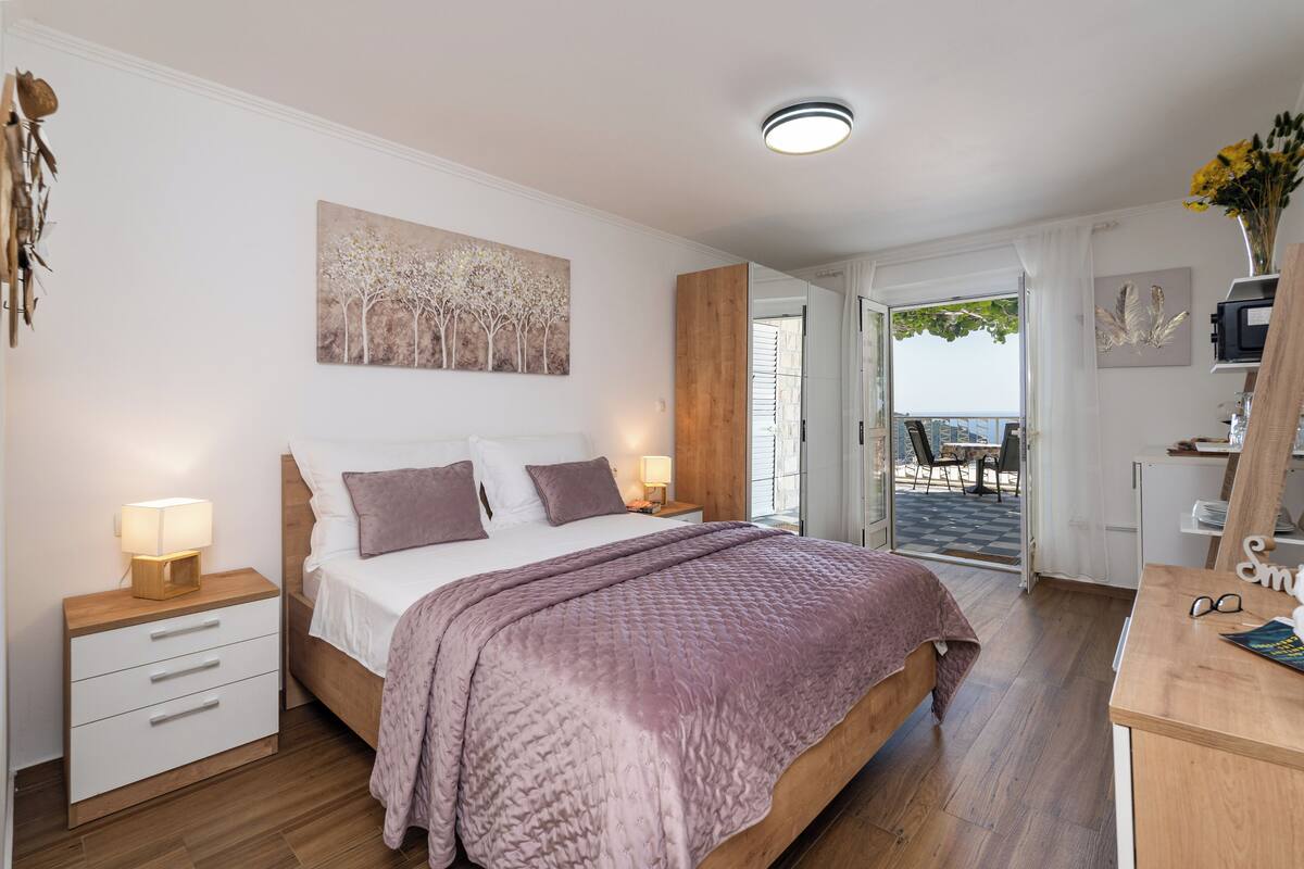 A bedroom with a bed, bedside tables, a painting, and a view of the outdoors.