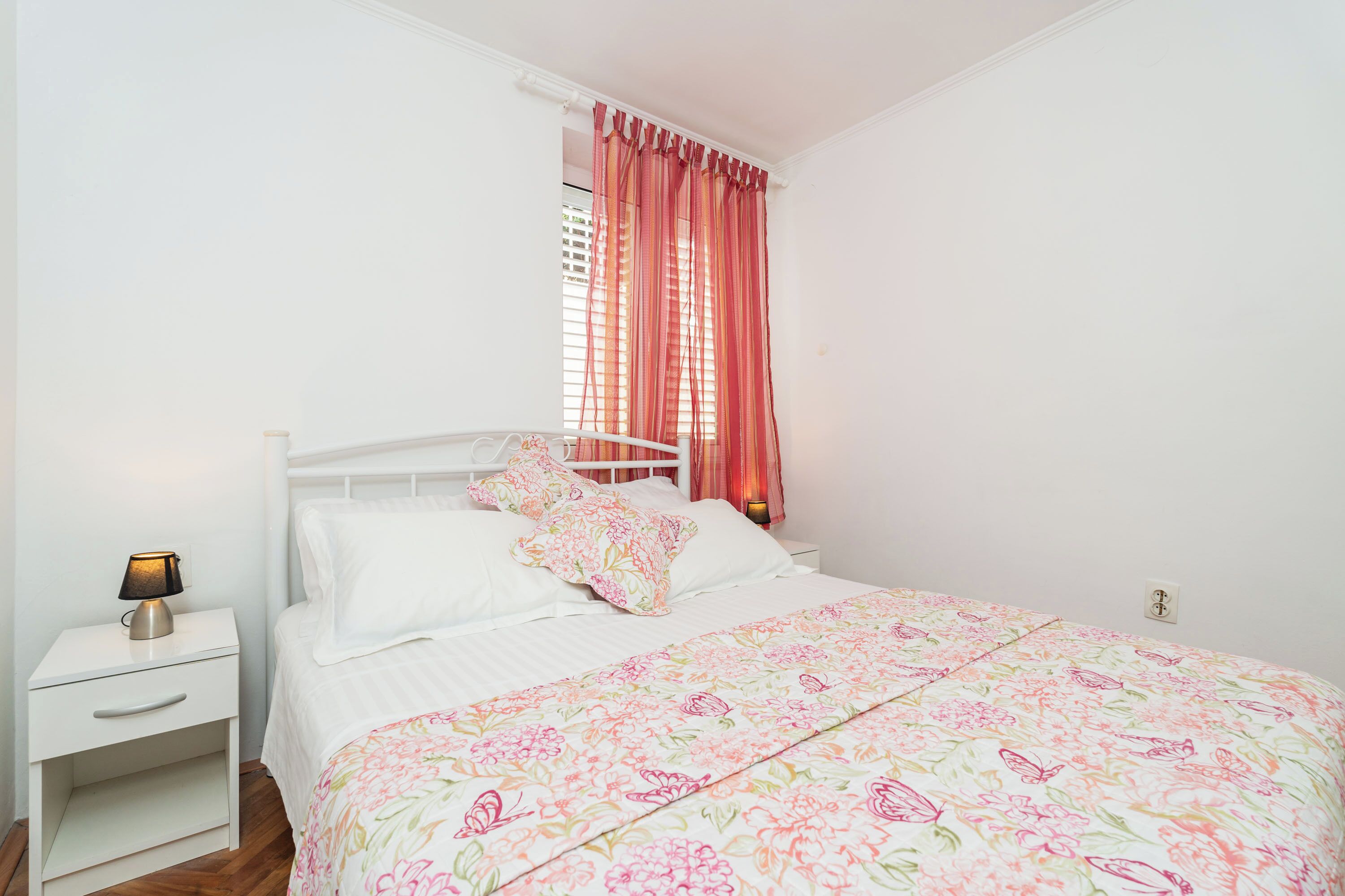 A bedroom with a bed, white nightstand, and a lamp.