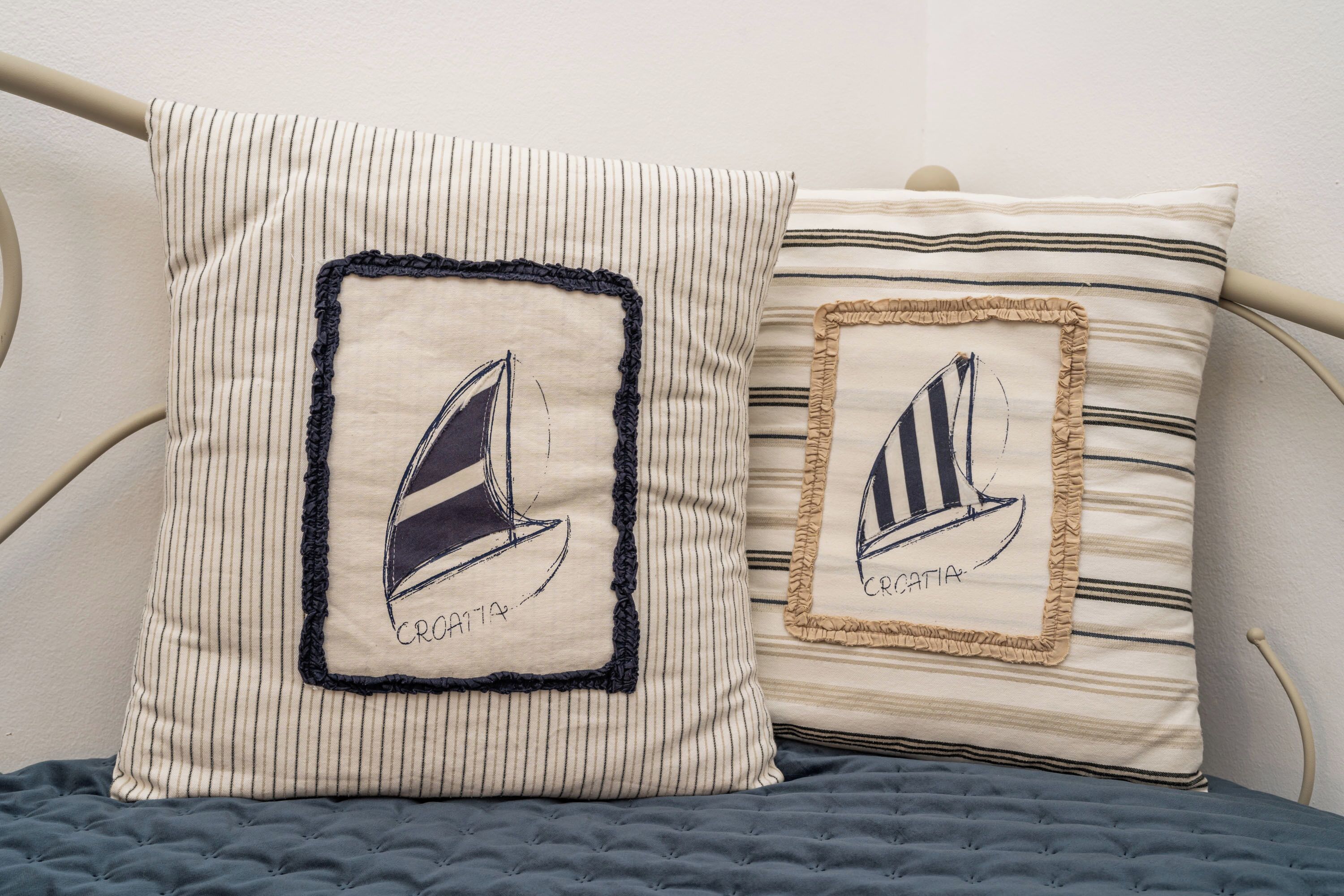 Two pillows with nautical designs on a bed with a metal frame.