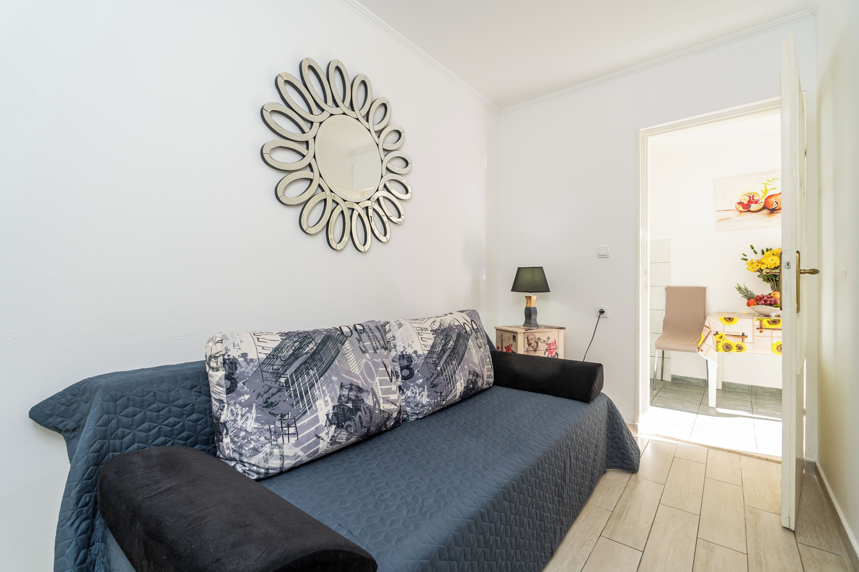 A bedroom with a bed, a decorative mirror, a lamp, and a view of a dining area.