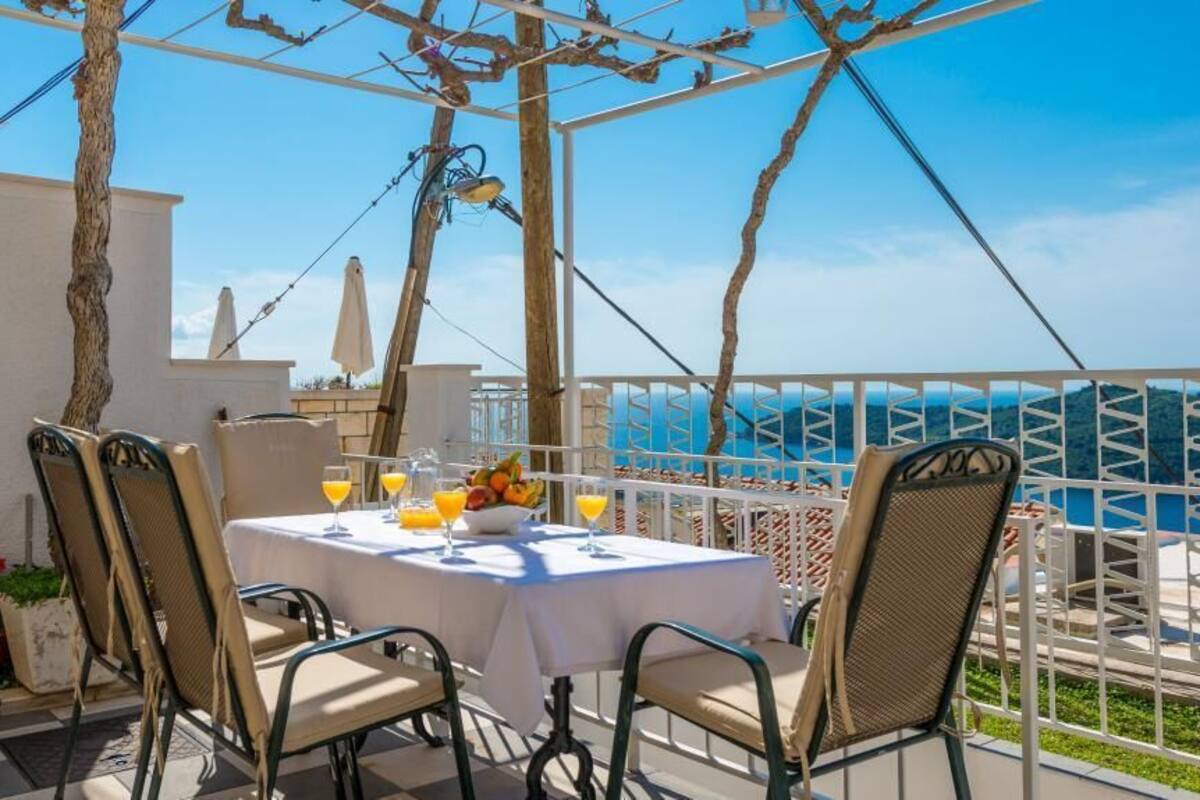 A terrace with a table set for two, outdoor chairs, a fruit bowl, and a view of the sea.