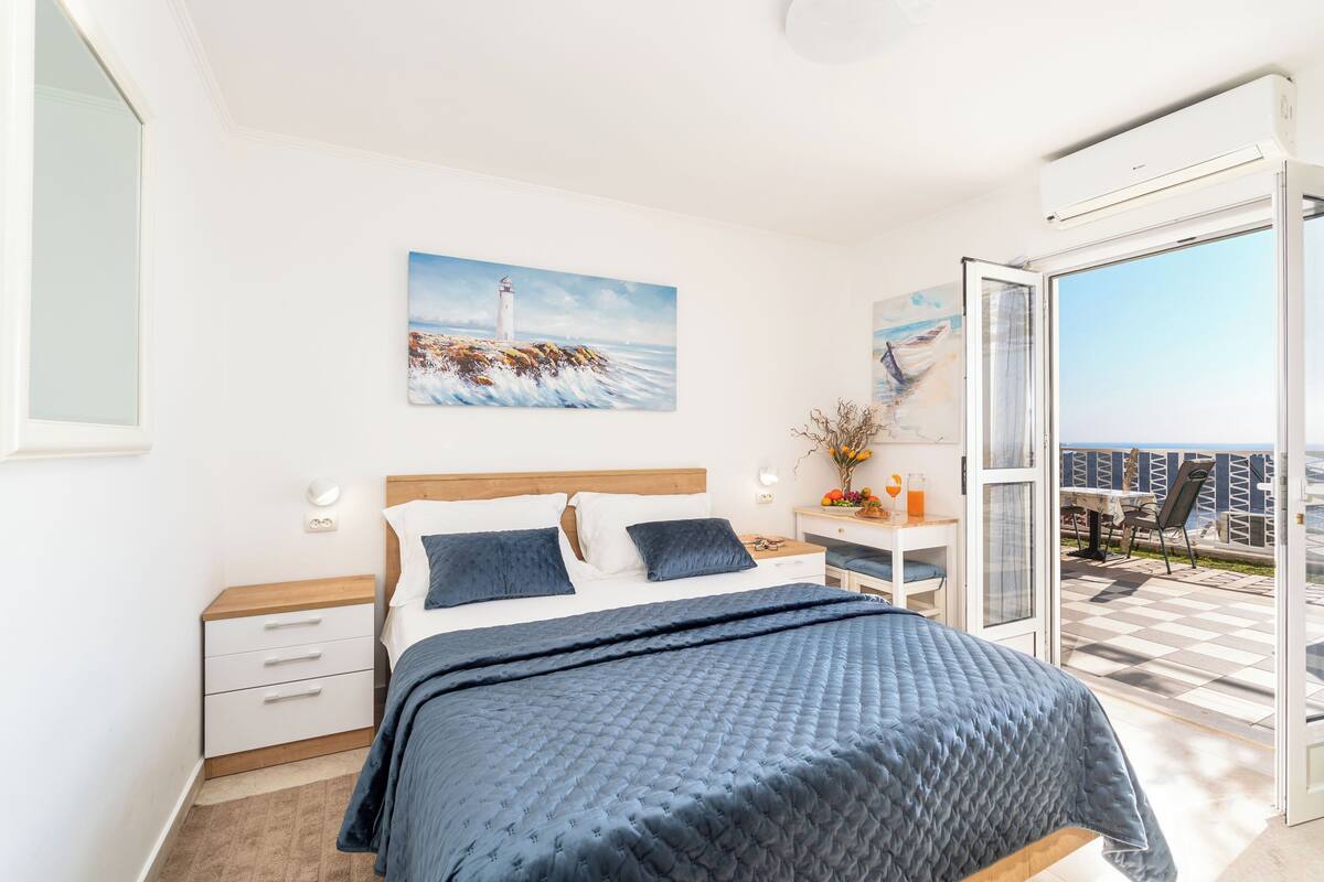A bedroom with a bed, a nightstand, a desk, and a view of the balcony.