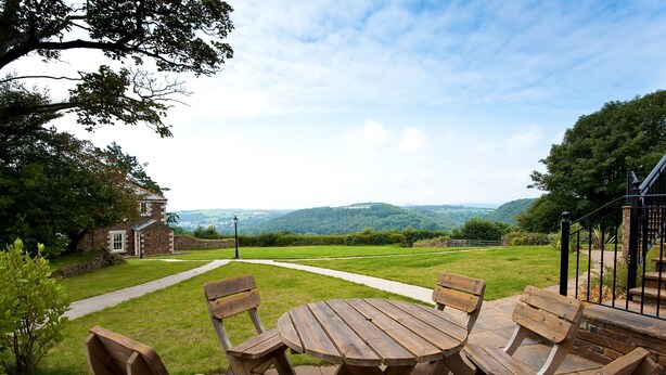 A patio with wooden furniture and a view of a rural landscape. - Green Acres Cottages (Par)