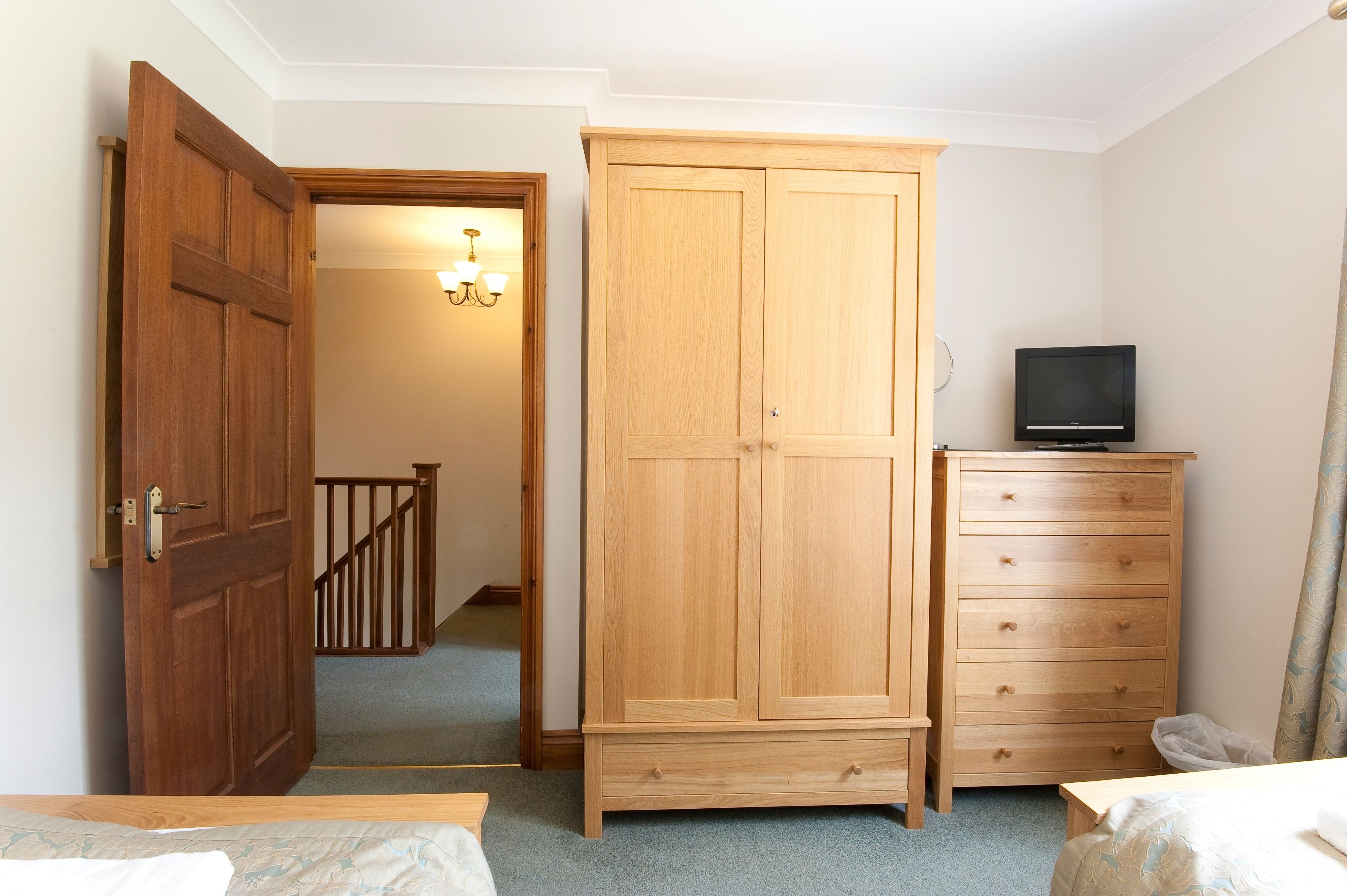 Une chambre à coucher avec une armoire en bois, un téléviseur posé sur une commode et un lit.