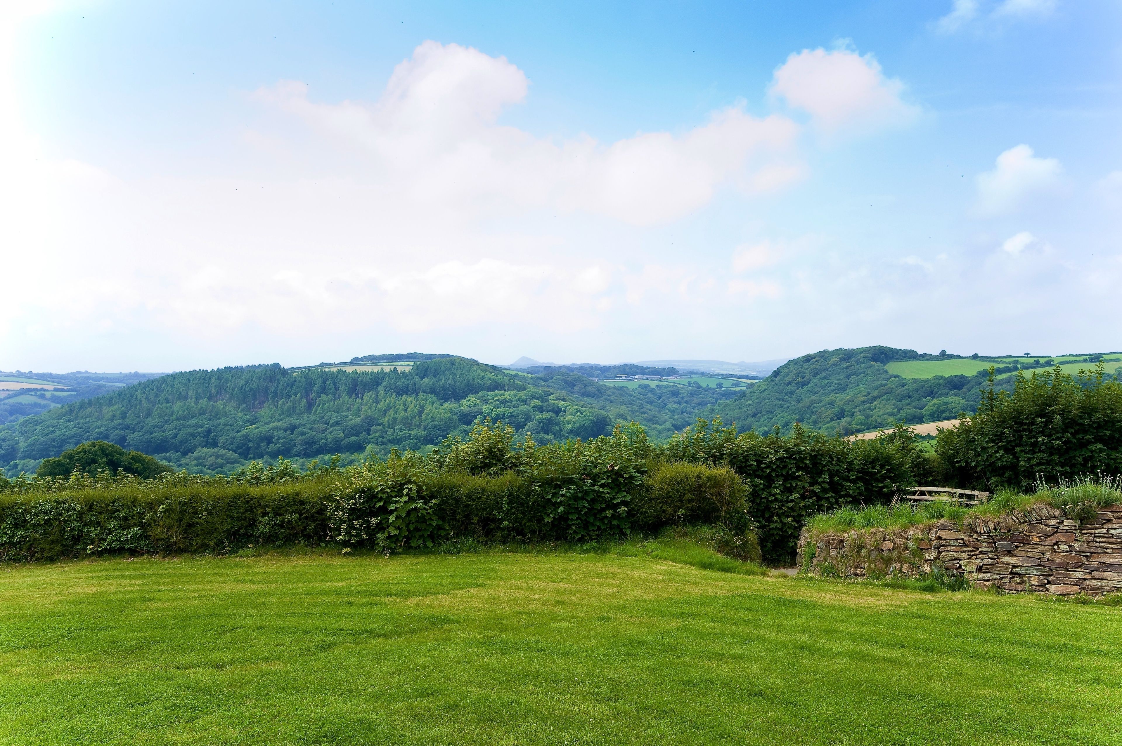 A grassy field with a stone wall and a stone building in the distance.