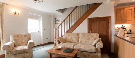 A living room with a sofa, armchair, and coffee table. A staircase leads to another room.