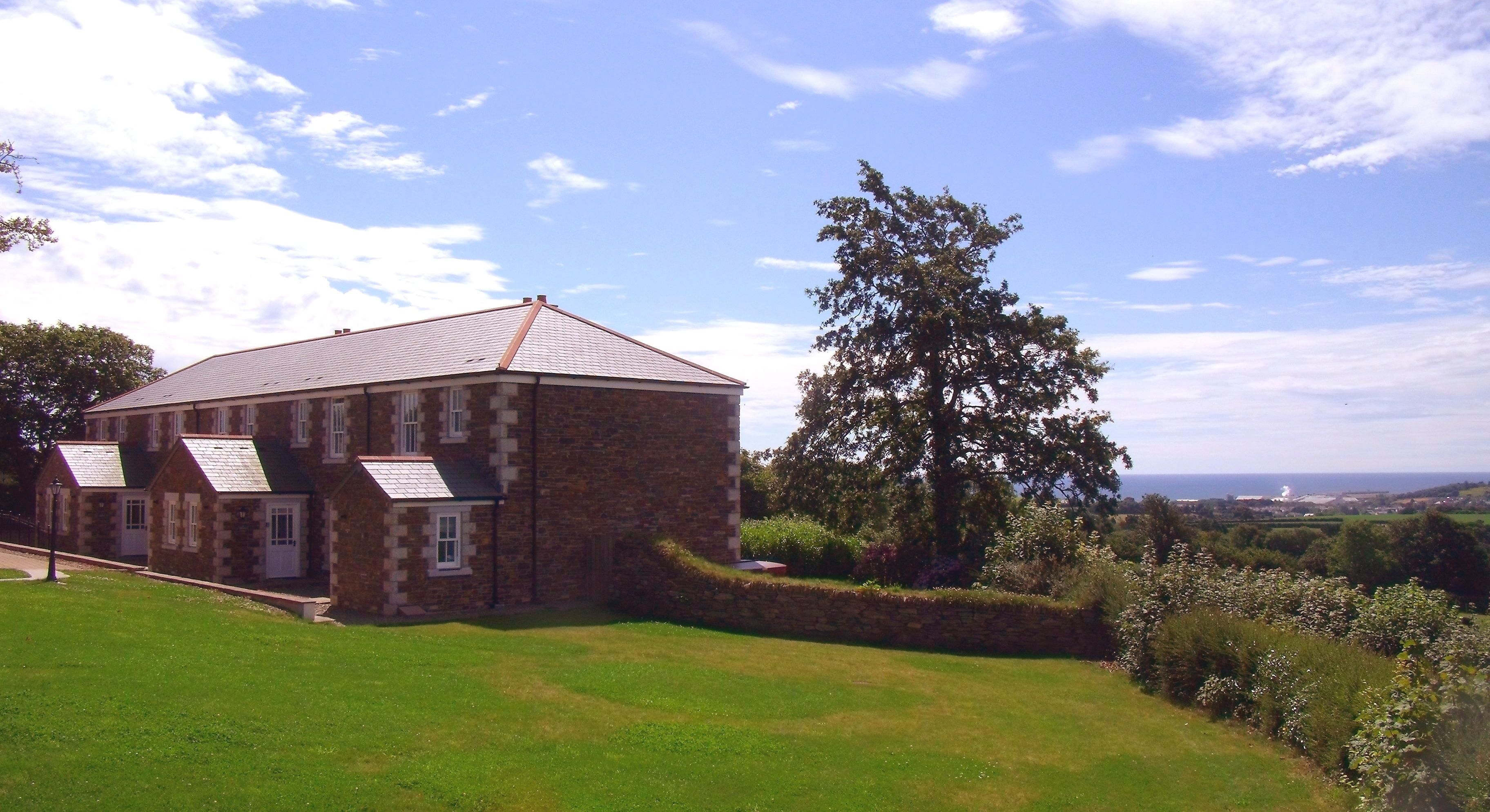A stone building with a sloped roof, surrounded by a well-maintained lawn and a large tree.