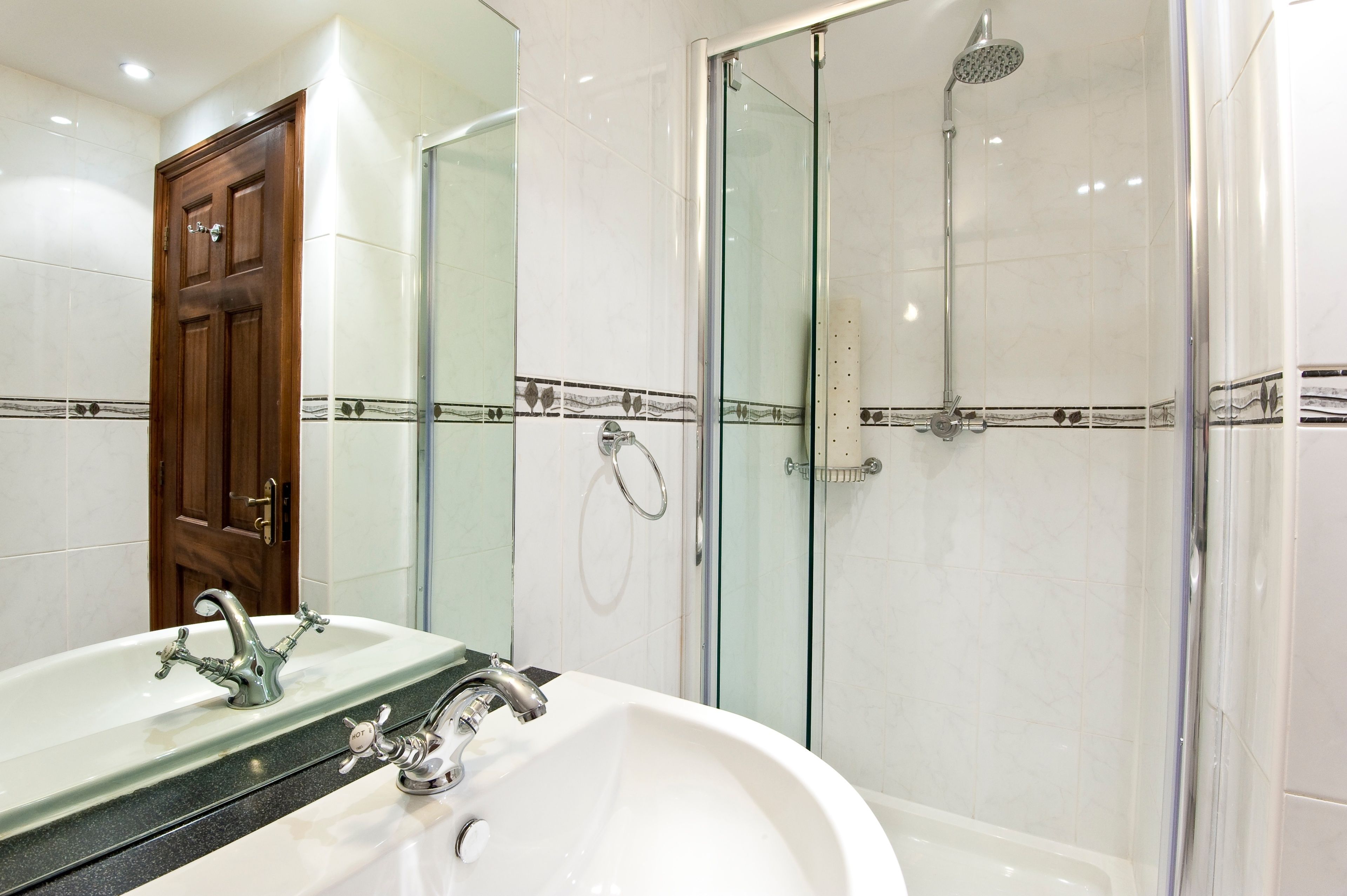 Een badkamer met een wastafel, spiegel, douche en glazen deur.