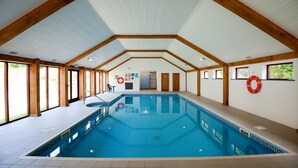 An indoor swimming pool with a high ceiling, wooden beams, and large windows. - Green Acres Cottages (Par)