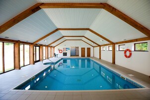Una piscina interior con techo alto, vigas de madera y grandes ventanales.