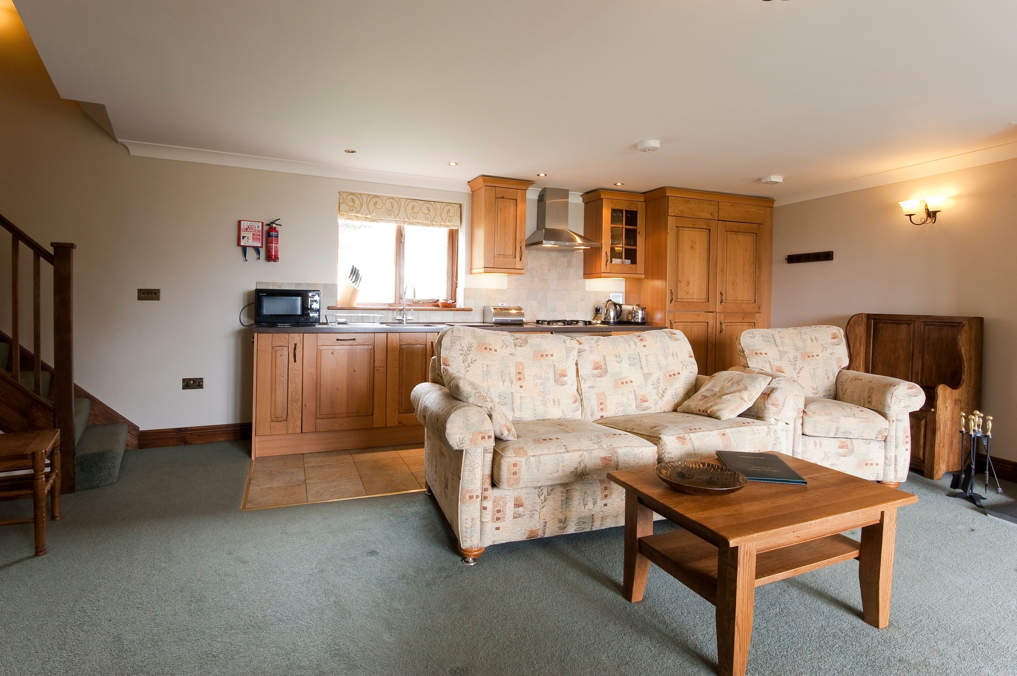 A living room with a sofa, a coffee table, and a kitchen area with wooden cabinets and a microwave.