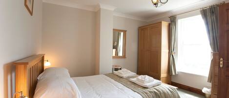 A neatly made bed with a lamp, a wooden wardrobe, and a window with curtains.