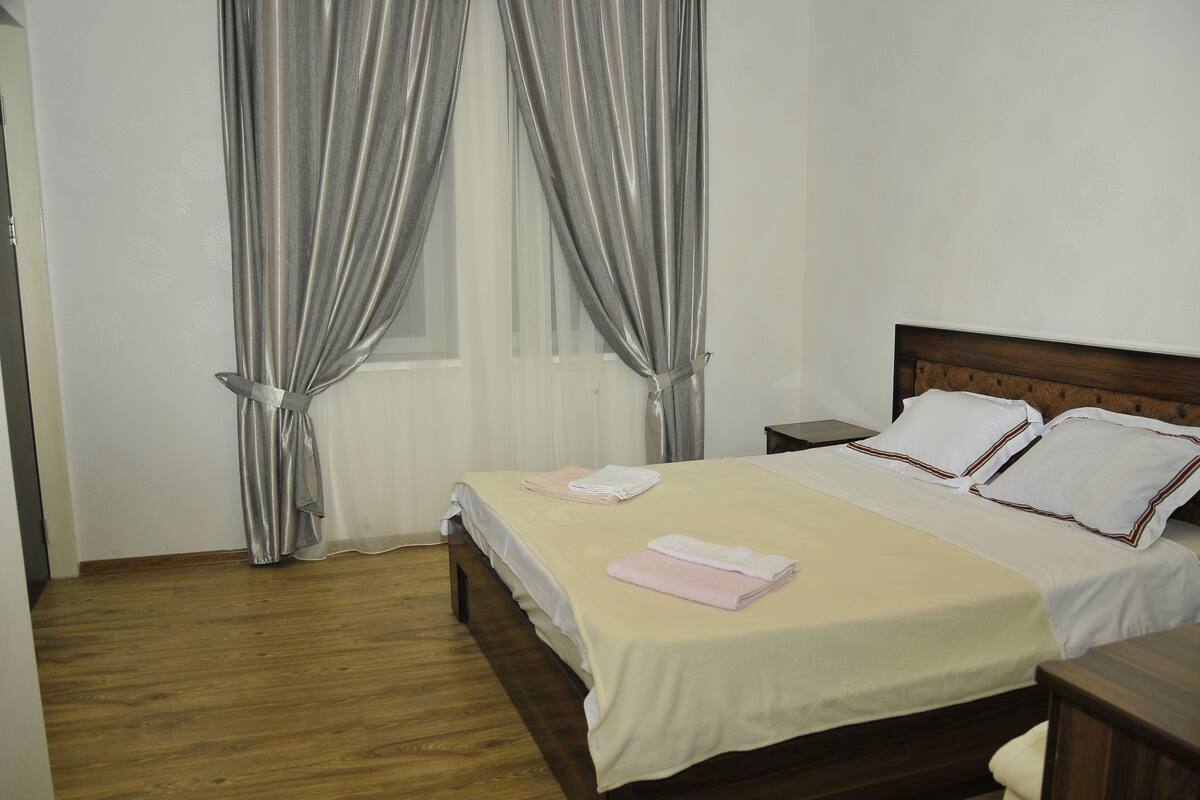 A neatly made bed with white and pink linens, a wooden headboard, and a wooden floor.