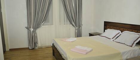 Una cama bien tendida con ropa de cama blanca y rosa, un cabecero de madera y suelo de madera.
