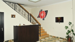A staircase with a wooden handrail and black balusters, a dark wooden desk, a potted plant, and a television mounted on the wall. - Alma-Ata Hotel (Borjomi)