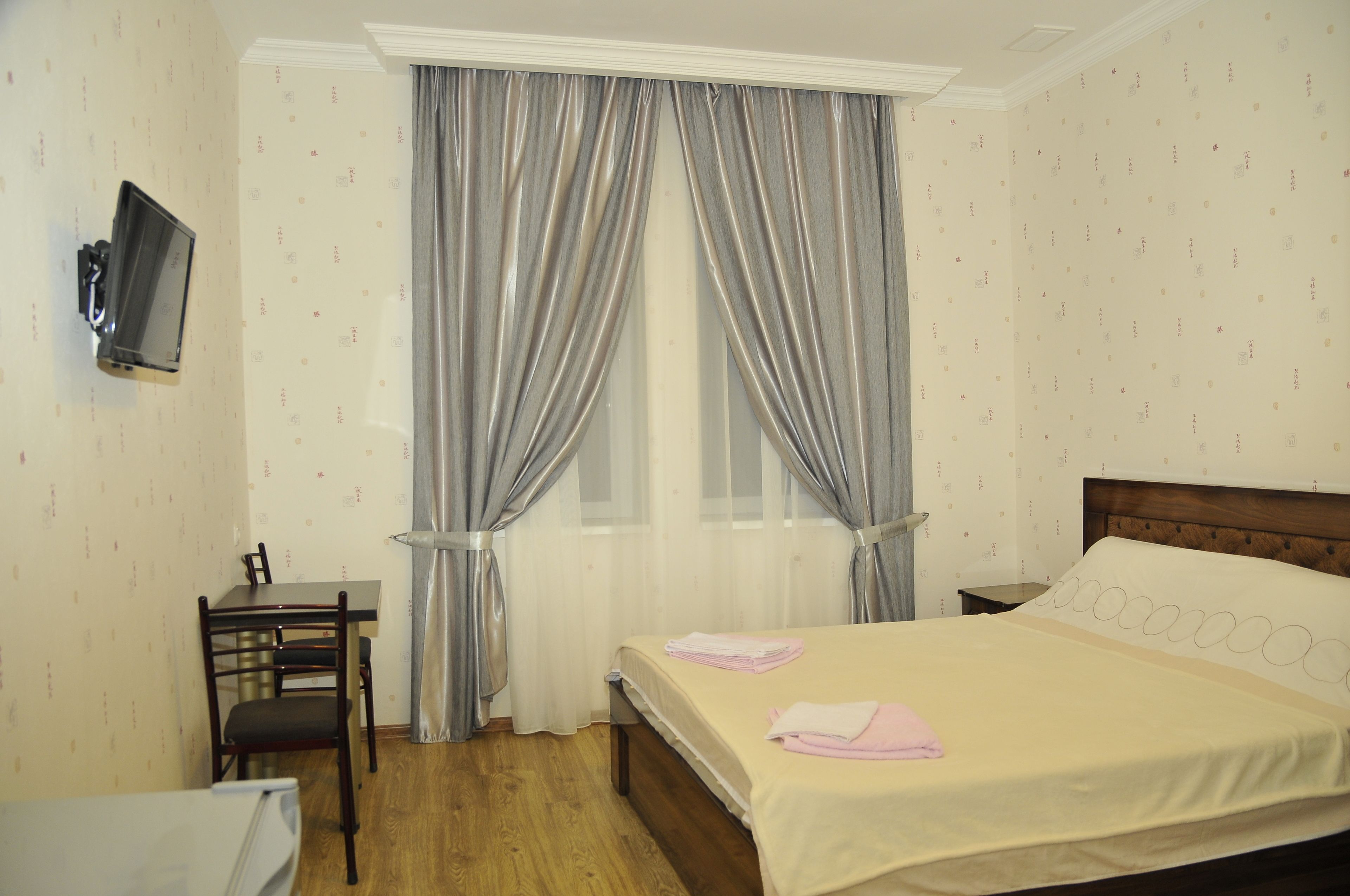 A hotel room with a bed, a desk, and a television on the wall.