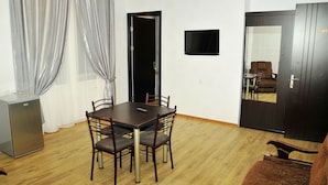 A dining area with a wooden table and chairs, a television on the wall, and a door with a number. - Alma-Ata Hotel (Borjomi)