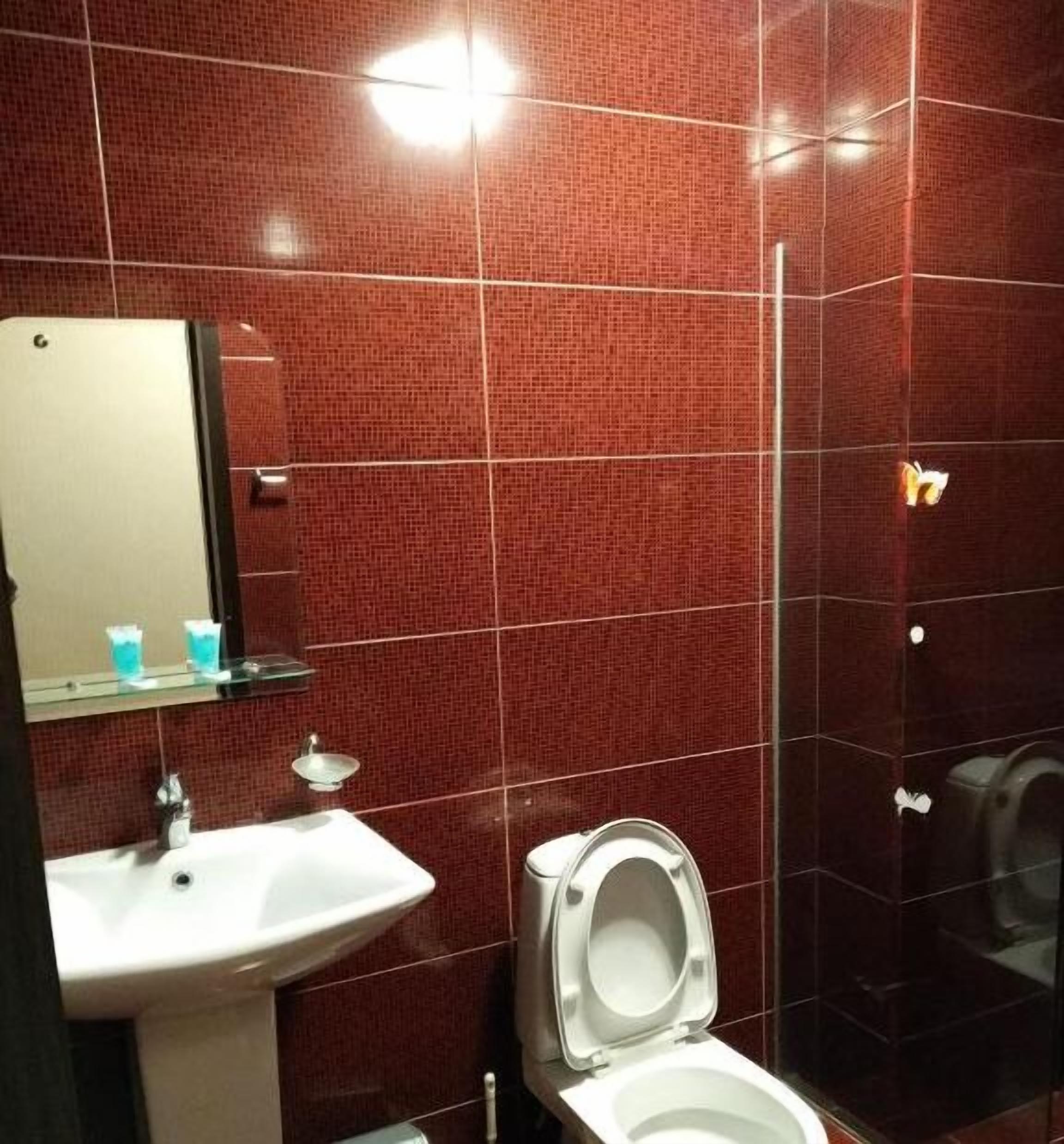 Ein Badezimmer mit weißem Waschbecken, Spiegel und Toilette. Die Wände sind mit roten Fliesen versehen.